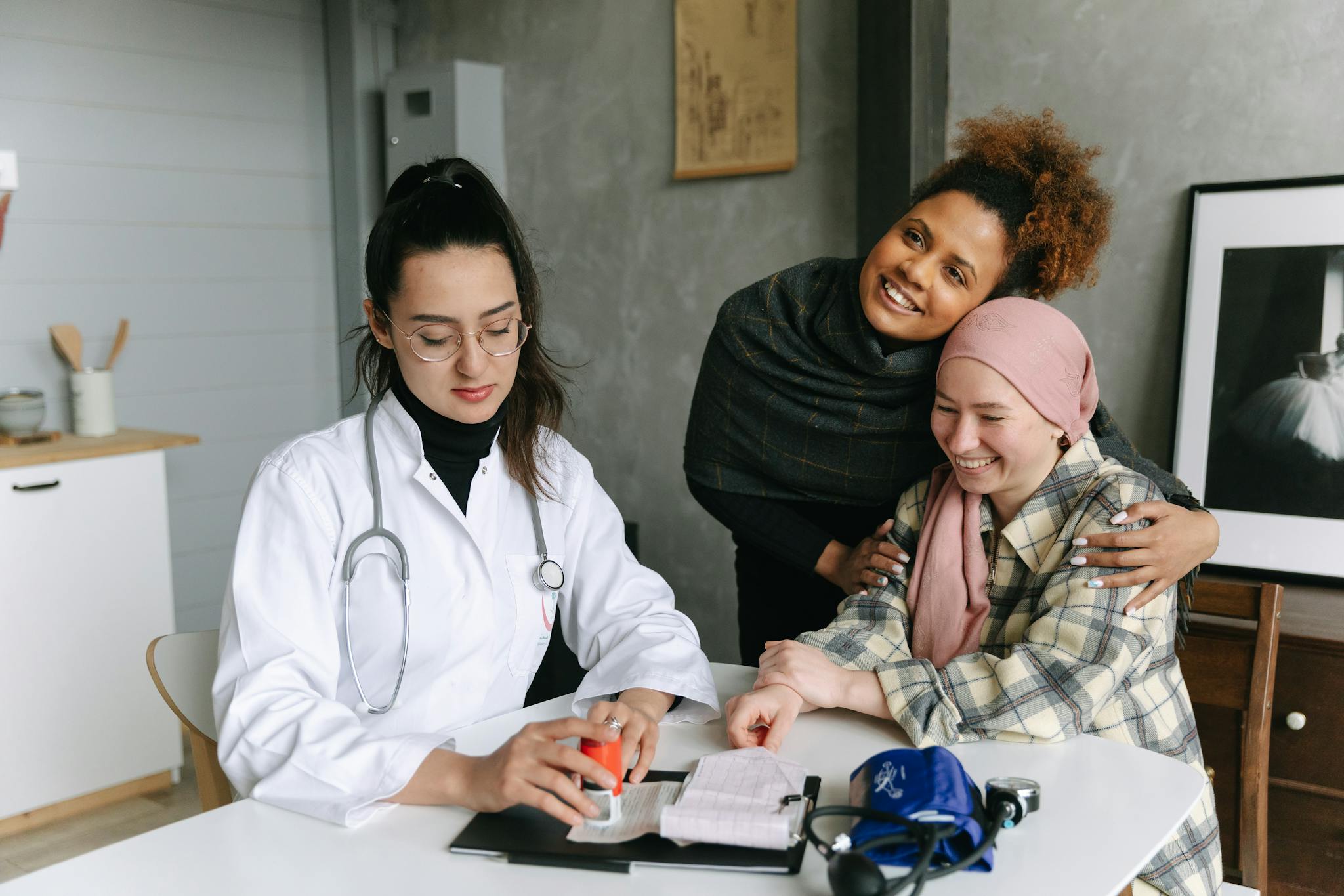 A doctor consults a cancer patient and her supportive friend in a warmly lit clinic room.