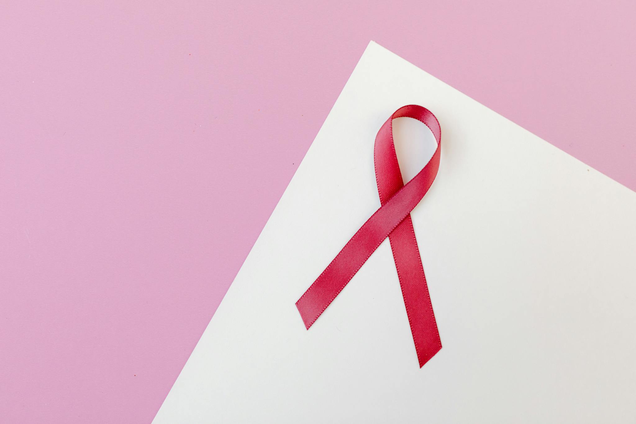 Close-up of a pink awareness ribbon on a white paper with a pink background, symbolizing breast cancer awareness.